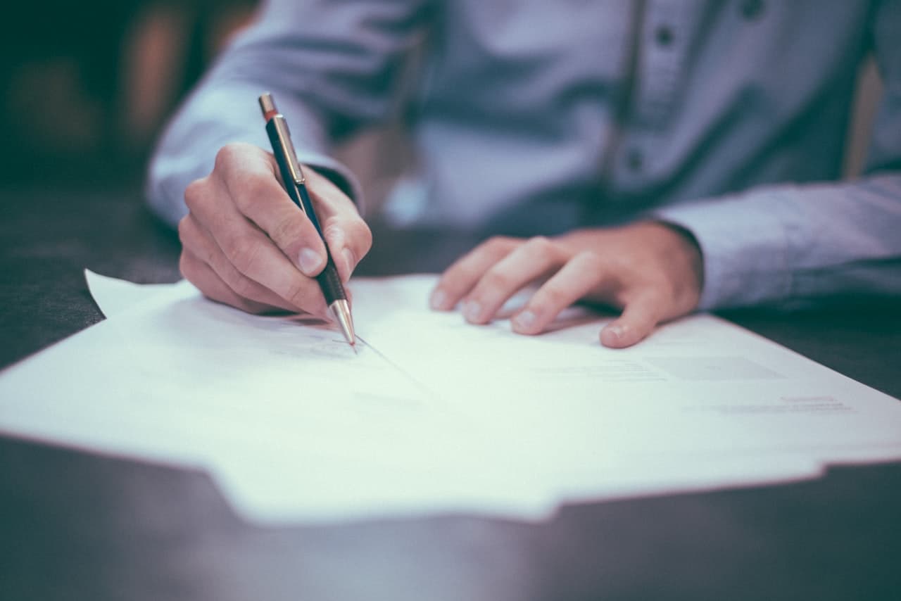 Hands signing financial paperwork at a desk